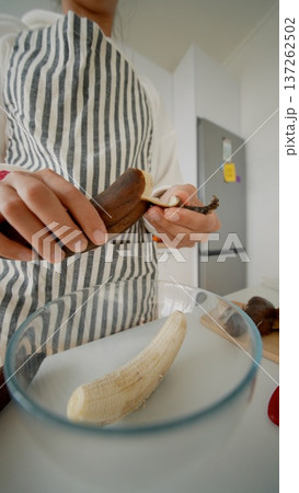 Hands in striped apron mash ripe banana on wooden board for dessert baking Hands in striped apron mash ripe banana on wooden board for dessert baking 137262502