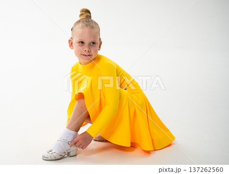 Little dancer with cochlear implant adjusting shoe on white floor. Copy space. Inclusion, discipline, and awareness of hearing technology in early childhood art. Little dancer with cochlear implant adjusting shoe on white floor. Copy space. Inclusion, discipline, and awareness of hearing technology in early childhood art. 137262560