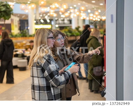 A mother and her teenage daughter are walking through a shopping mall. A mother and her teenage daughter are walking through a shopping mall. 137262949