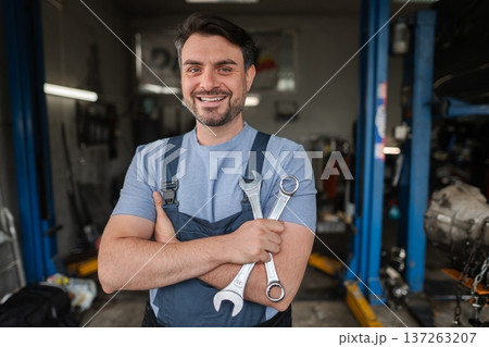 Confident mechanic holding wrenches in auto repair shop smiling 137263207
