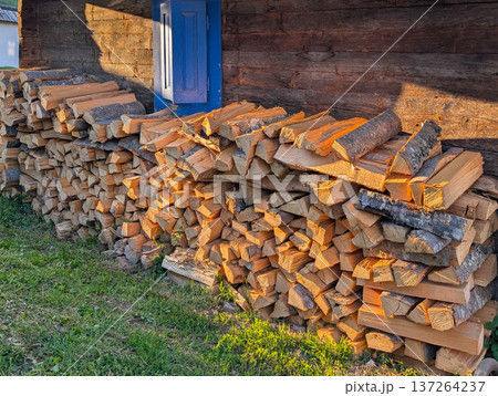 Piles of firewood near wooden house with colorful windows. Village lifestyle and architecture. Piles of firewood near wooden house with colorful windows. Village lifestyle and architecture. 137264237
