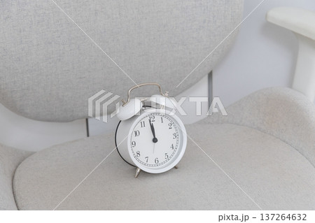 White alarm clock on chair. Minimalism, clarity, and peaceful rhythm of slow living lifestyle. Copy space White alarm clock on chair. Minimalism, clarity, and peaceful rhythm of slow living lifestyle. Copy space 137264632