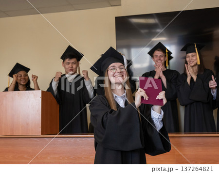 Happy Caucasian woman holds red diploma and classmates support her.  137264821