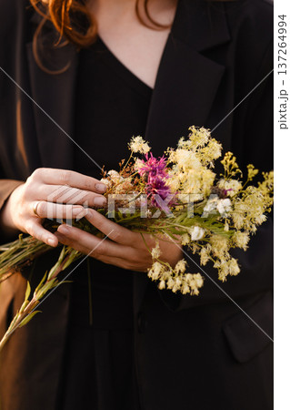 Young woman holding bouquet of wildflowers in black coat close up 137264994