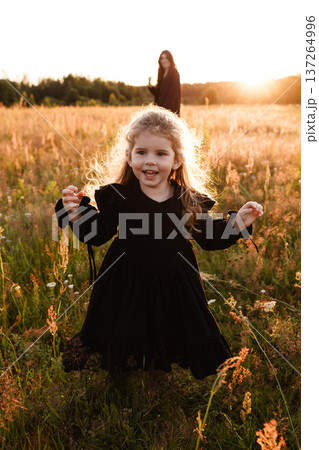 Little girl running in meadow at sunset with mother in background Little girl running in meadow at sunset with mother in background 137264996