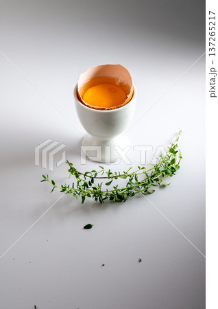 Fresh egg cracked open with bright yellow yolk, served in white ceramic egg cup on clean white background. Fresh egg cracked open with bright yellow yolk, served in white ceramic egg cup on clean white background. 137265217