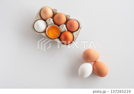 Natural farm eggs arranged in carton, one egg cracked to reveal raw yolk. Minimal composition. Natural farm eggs arranged in carton, one egg cracked to reveal raw yolk. Minimal composition. 137265219