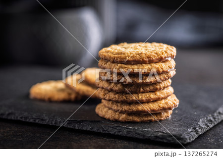 Stack of oatmeal cookies on slate with some placed beside it in a kitchen setting during daylight hours 137265274