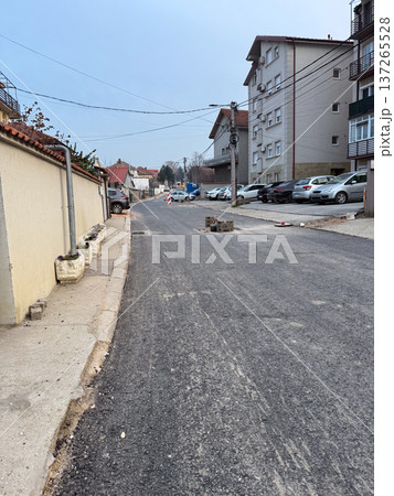 Empty suburban street with fresh asphalt and residential houses under cloudy sky. Urban infrastructure, road maintenance, neighborhood development, and everyday city transport environment 137265528