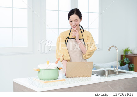 キッチンでパソコンを見ながら料理をする主婦 キッチンでパソコンを見ながら料理をする主婦 137265913