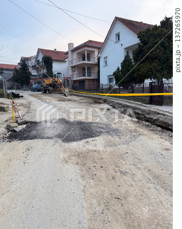 Residential street with damaged asphalt road and visible construction work in suburban neighborhood. Urban infrastructure repair, civil engineering development, municipal maintenance and 137265970