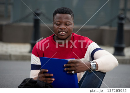 Handsome college man reading notes in notebook on campus. Handsome college man reading notes in notebook on campus. 137265985