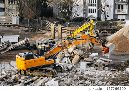 Urban Building Demolition Site: Excavator Spraying Water Over Concrete Rubble And Debris To Reduce Dust During Controlled Demolition Work 137266390