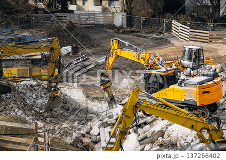 Urban Building Demolition Site: Excavator Spraying Water Over Concrete Rubble And Debris To Reduce Dust During Controlled Demolition Work 137266402