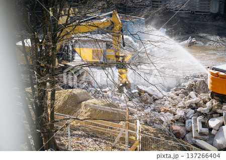 Urban Building Demolition Site. Residential Construction Site Behind Apartment Windows: View Through Glass Showing Excavator, Demolition Debris, Water Spray, And Urban Renovation Activity In A 137266404