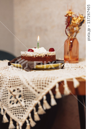 Chocolate birthday cake with a burning candle on a lace tablecloth in a moody vintage interior. Festive still life for holiday and celebration designs 137267405