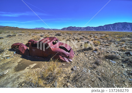 Abandoned Rusted Car in Desert Landscape with Distant Mountain Range under Blue Sky Abandoned Rusted Car in Desert Landscape with Distant Mountain Range under Blue Sky 137268270