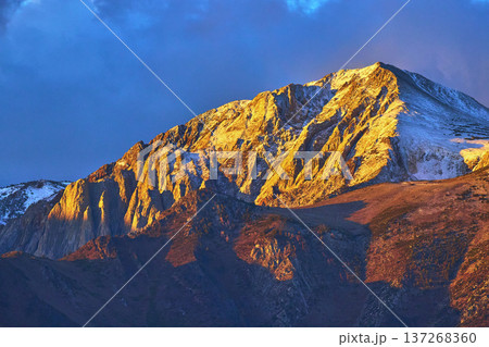 Sunrise Light on Snow Capped Mountain Peak with Dramatic Sky and Rocky Slopes 137268360