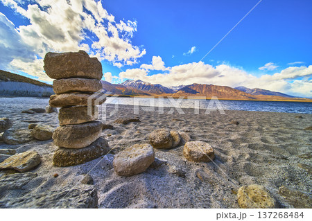 Rock Cairn on Sandy Shore with Mountain and Lake View Under Blue Sky 137268484