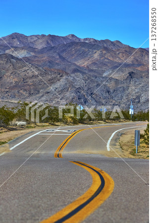 Winding Mojave Desert Road and Rugged Mountains Under Clear Blue Sky California Winding Mojave Desert Road and Rugged Mountains Under Clear Blue Sky California 137268550