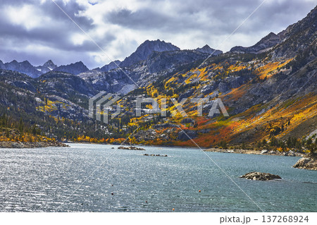 Mountain Lake with Dramatic Fall Foliage and Granite Peaks Under Cloudy Sky 137268924