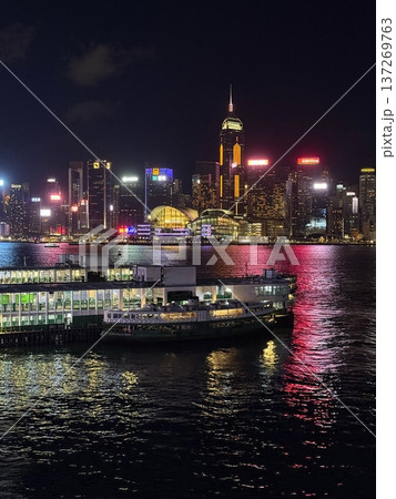 Hong Kong skyline at night with ferries and illuminated skyscrapers reflecting on the water Hong Kong skyline at night with ferries and illuminated skyscrapers reflecting on the water 137269763