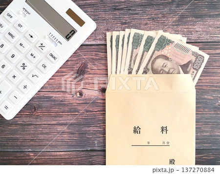 木製テーブルに置いた電卓と給料袋に入った紙幣 木製テーブルに置いた電卓と給料袋に入った紙幣 137270884