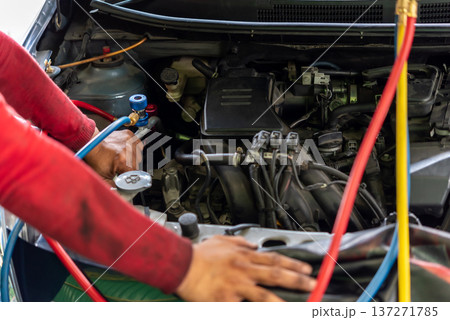 Mechanic checking car air conditioning system with manifold gauge set under open hood during vehicle maintenance repair in auto service garage close up engine bay work 137271785