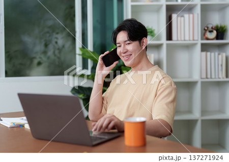 Remote Work. Young man engaged in a phone call while working on a laptop at home. 137271924