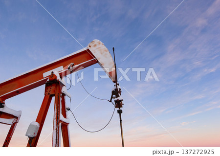Oil Pumpjack's horsehead against blue and pink sky. Oil Pumpjack's horsehead against blue and pink sky. 137272925