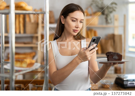 Female customer takes a photo of a sweet pie using a smartphone in the interior of private bakery Female customer takes a photo of a sweet pie using a smartphone in the interior of private bakery 137273842