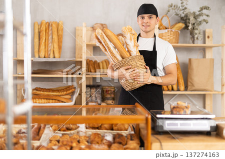 Young smiling man baker offers to buy fresh delicious baguettes 137274163