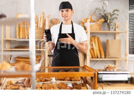 Portrait of friendly male baker with smartphone in hands in bakery interior 137274180