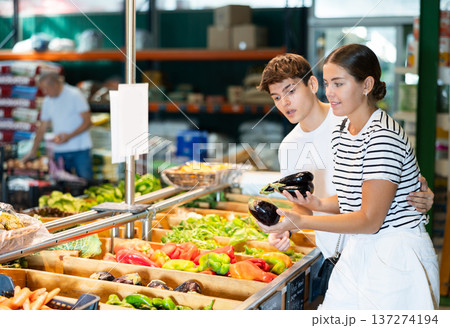 Cheerful young couple choosing ripe eggplants in farm store Cheerful young couple choosing ripe eggplants in farm store 137274194