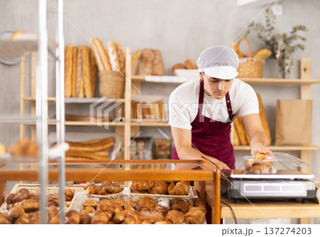 Young male seller puts disposable plastic box with buns on scales 137274203