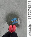 雨の日の水たまりに立つ赤いスニーカーの足元写真 137274243