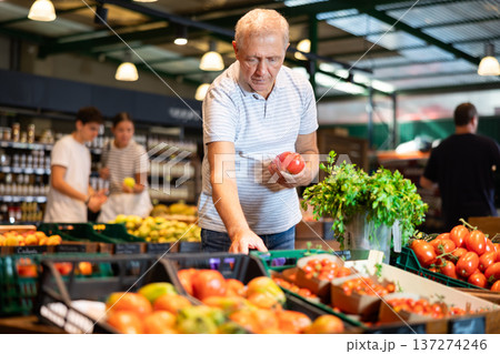 Elderly man chooses tomatoes in grocery store 137274246