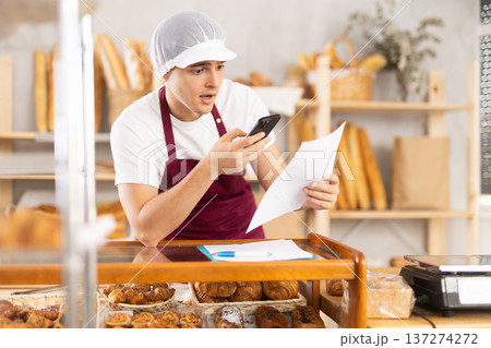 Bakery guy employee holds paper documents in hands, photographs report and sends it to tax office Bakery guy employee holds paper documents in hands, photographs report and sends it to tax office 137274272