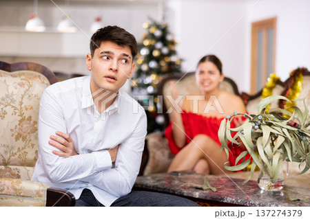 Displeased young European man and woman in red dress yelling at each other on sofa during preparations for New Year in living room Displeased young European man and woman in red dress yelling at each other on sofa during preparations for New Year in living room 137274379