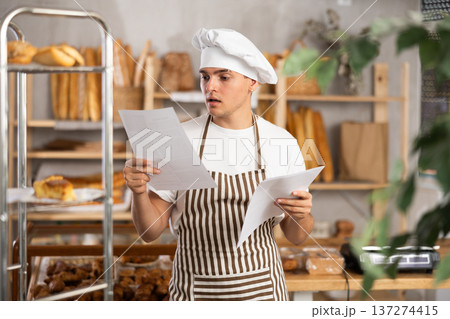 Focused young bakery worker checking order form Focused young bakery worker checking order form 137274415