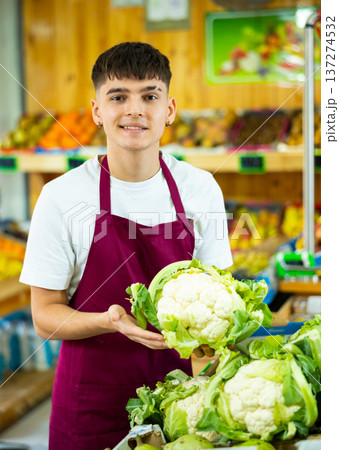 Friendly young seller man in apron demonstrating cauliflower in shop 137274532
