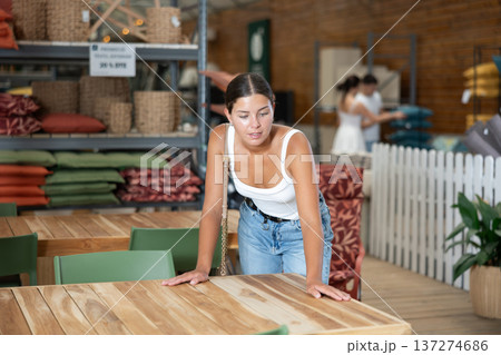 Interested girl choosing wooden table in garden furniture store Interested girl choosing wooden table in garden furniture store 137274686