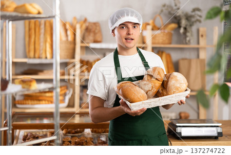 Smiling young baker presenting fresh baked bread in bakery 137274722