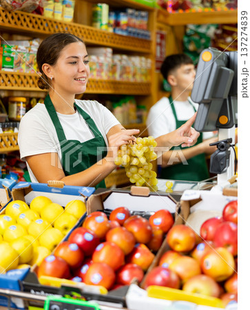 Smiling european female seller weighing grape in supermarket Smiling european female seller weighing grape in supermarket 137274839