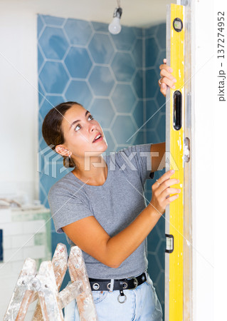 Portrait of a young woman using a spirit level on the bathroom wall Portrait of a young woman using a spirit level on the bathroom wall 137274952