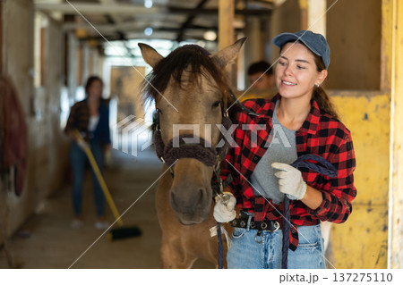 Portrait of smiling woman horse farm worker standing at stable 137275110