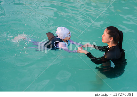 preschool child girl in life jacket learning to swim with mother in swimming pool 137276381