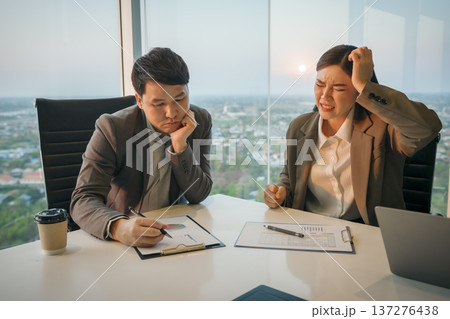 two business partners meeting and looking at documents with stressed and tired expressions in office 137276438