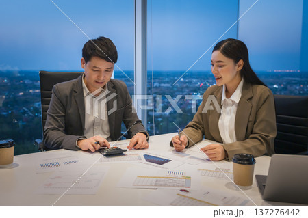 two business colleagues meeting and discussing financial reports and using calculator to data analysis in office at night two business colleagues meeting and discussing financial reports and using calculator to data analysis in office at night 137276442