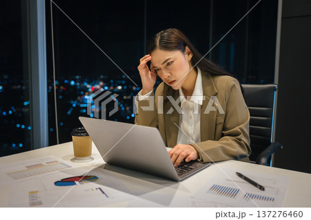 stressed businesswoman headache while working on laptop in business office with city lights background at night 137276460